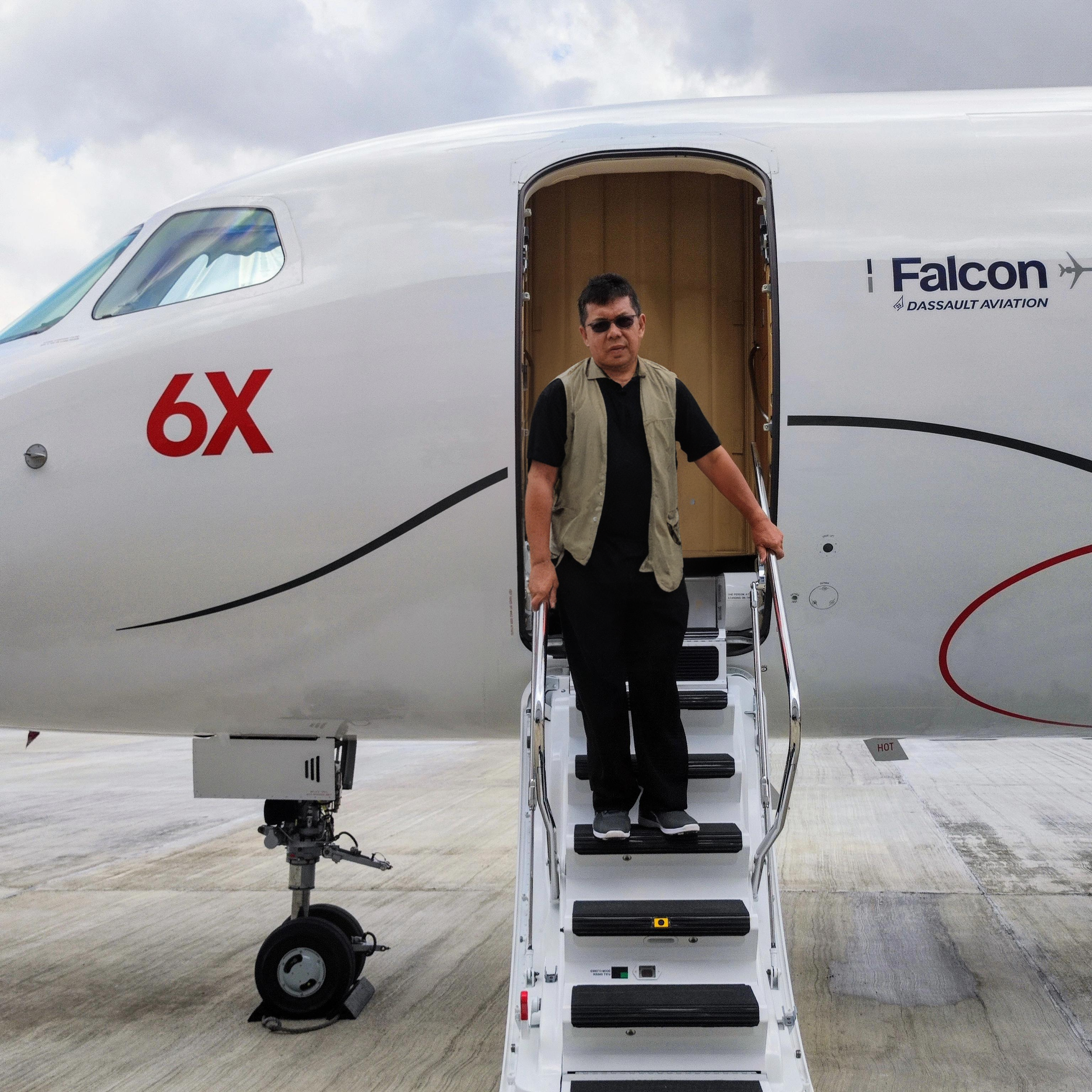 A man confidently steps down the stairs of a sleek Falcon 6X private jet, showcasing the advanced features of the aircraft. The image, created using Stable Assistant's Inpaint tool, demonstrates the software's ability to seamlessly blend realistic elements into the scene, enhancing the overall visual appeal and detail of the composition.